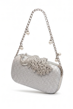 The Pearl Chain Handbag is a sparkling silver evening bag featuring a chain shoulder strap, pearls, and a jeweled flower and leaf design on the front.