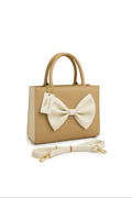 The Beige Bow Shoulder Bag is a small beige leather bag featuring rounded handles, a large cream bow accent on the front, a matching detachable strap, and a TBM Timeless by M tag.