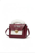 The Burgundy Faux Fur Handbag is a compact maroon crossbody with a white flap, gold clasp, adjustable strap, and white faux fur handle, shown against a white background.