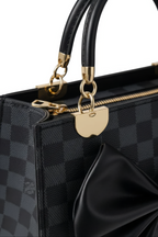 Close-up of the Nocturne Bow Handbag: a luxury black leather bag with a black checkered pattern, gold hardware, black handles, a large side bow accent, and a detachable shoulder strap for versatile carrying.