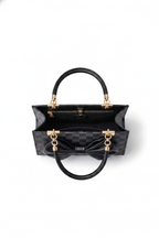 The Nocturne Bow Handbag, shown open from a top view on a white background, features black leather, gold hardware, a checkered pattern, large bow detail, top handle, and a detachable shoulder strap for versatile styling.